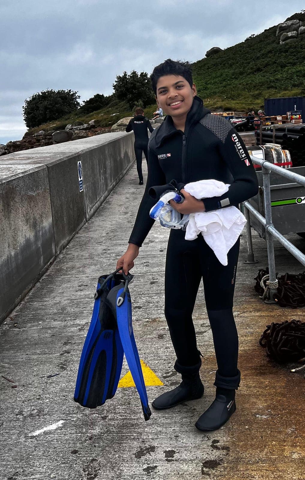 Darsh Shhaparia in a wetsuit holding fins at a dive site